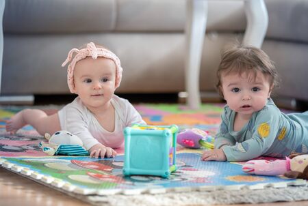 cute twins, baby girl and baby boy playing with toys by the homeの写真素材