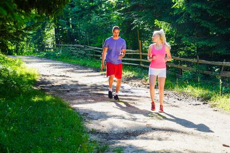 Running fitness couple of runners doing sport on road outdoor. Active living man and woman jogging training cardio in summer outdoors nature.の写真素材