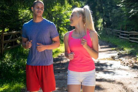 Running fitness couple of runners doing sport on road outdoor. Active living man and woman jogging training cardio in summer outdoors nature.の写真素材