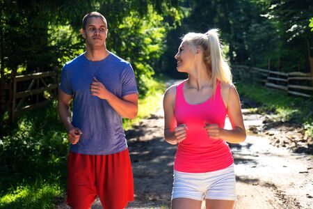 Running fitness couple of runners doing sport on road outdoor. Active living man and woman jogging training cardio in summer outdoors nature.の写真素材