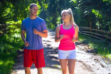 Running fitness couple of runners doing sport on road outdoor. Active living man and woman jogging training cardio in summer outdoors nature.の写真素材