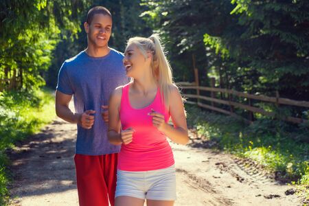 Running fitness couple of runners doing sport on road outdoor. Active living man and woman jogging training cardio in summer outdoors nature.の写真素材