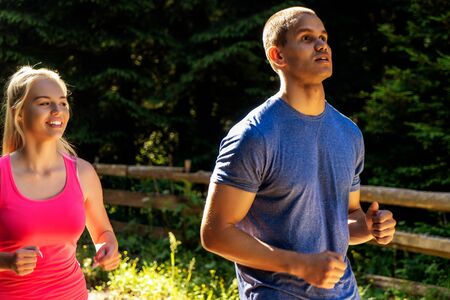 Running fitness couple of runners doing sport on road outdoor. Active living man and woman jogging training cardio in summer outdoors nature.の写真素材