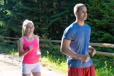 Running fitness couple of runners doing sport on road outdoor. Active living man and woman jogging training cardio in summer outdoors nature.の写真素材