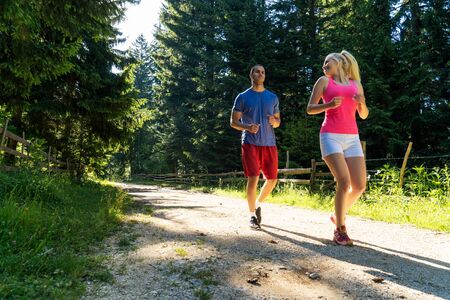 Running fitness couple of runners doing sport on road outdoor. Active living man and woman jogging training cardio in summer outdoors nature.の写真素材