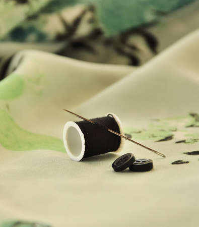 Two buttons, needle and thread on colored cloth