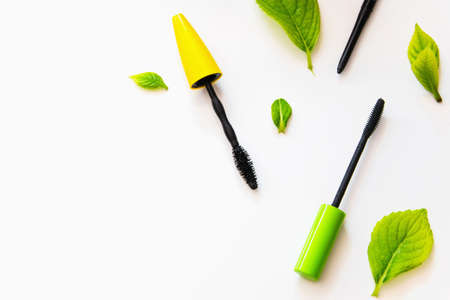 Top view of a mascara brushes and an eye pencil on a white background with green leavesの写真素材