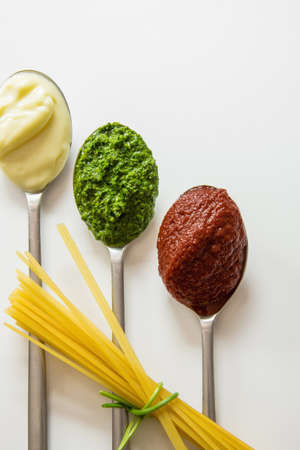 Spaghetti and three spoons with different condiments - tomato sauce, mayonnaise and pestoの写真素材