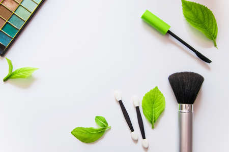 Top view of make-up products on white background with green leavesの写真素材
