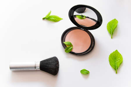Face powder and a brush on white background with green leaves
