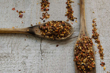 Two spoons with chilli on wooden background