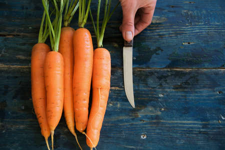 Top view of woman hands peeling with fresh carrots on rustic blue tableの写真素材