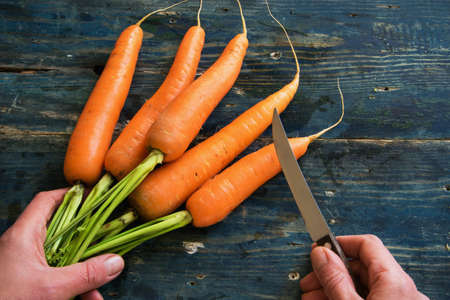 Top view of woman hands peeling with fresh carrots on rustic blue tableの写真素材