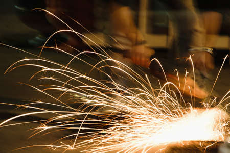 Worker with grinder, sparks while grinding iron. Low key photography, space for text