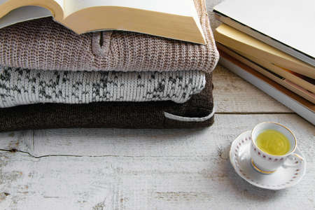Cozy warm knitted sweaters, books and cup of tea on wooden background with space for text. Concepts - fashion, comfortable time spent at home, rustic hygge life, relaxingの写真素材