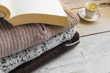 Warm knitted maxi sweaters, book and cup of tea on wooden background with space for text. Concepts - fashion, comfortable time spent at home, rustic hygge life, relaxingの写真素材