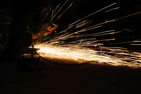 Worker with grinder, sparks while grinding iron. Low key photography, space for text