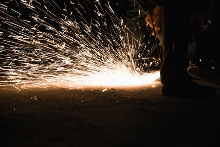 Worker with grinder, sparks while grinding iron. Low key photography, space for textの写真素材