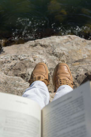 Above view of an adult person holding open book, sitting on the sea rocksの写真素材