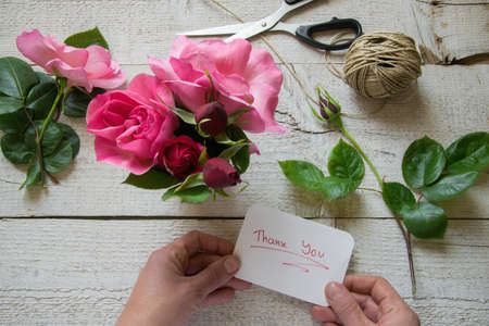 Top view of female decorator holding "Thank you" card, arranging roses on the wooden table, Concepts - fiorist, occupation, hobby, small businessの写真素材