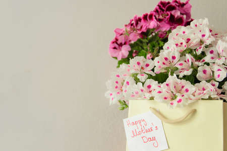 Paper bag with fresh flowers and greeting card for the Mother's day on the wooden table, space for...
