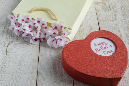 Paper bag with fresh flowers and heart box gift for the Mother's day on the wooden table, space for textの写真素材