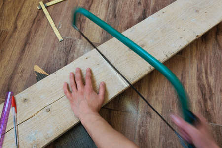 Top view of woman hands sawing a wooden plank indoors. Concepts - craft, carpentery, DIY, woodworkの写真素材