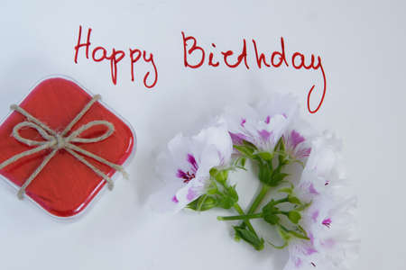 Happy birthday greeting card with gift box and fresh flowers on white background, space for textの写真素材