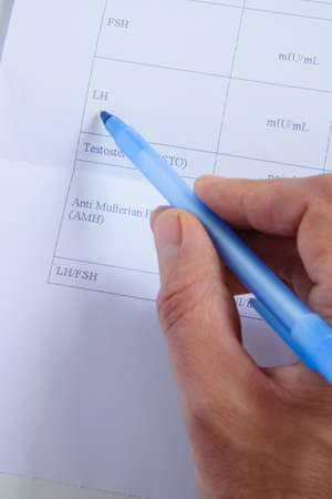 Top view of doctor hand consults blood tests list for female hormones / fertility. Healthy medical...