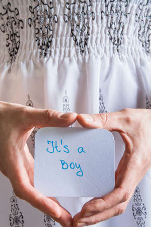 Front crop view of woman hands holding a white card with text "It's a boy", baby boy shower celebrationの写真素材