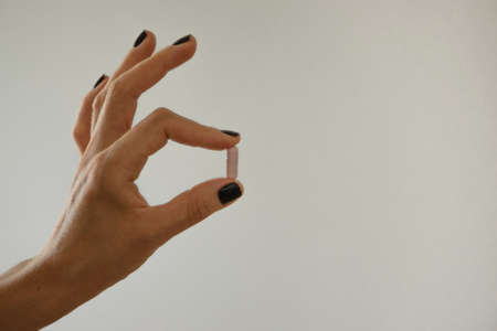 Isolated woman hand holding a pink pill, white background with space for text