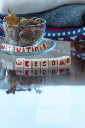 "Winter Welcome" text phrase, tea cup with acorns and pile of woolen sweaters on background, space for textの写真素材