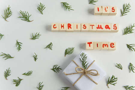 Top view of white handcraft gift box with "It's Chrismas time" text (wooden letters) and fresh fir branches on white background, seasonal celebration and eco-friendly conceptの写真素材