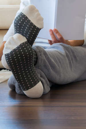 Cropped view of woman with pajamas sitting on the wooden floor at home and reading a book, everyday...