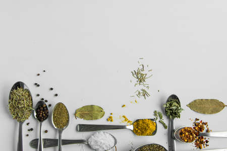 Spoons with various aromatic herbs and spices on white background, space for text. Different flavouring condiment choiceの写真素材