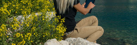 Crop view of young adult business woman working with digital tablet sitting at seaside cliff edge