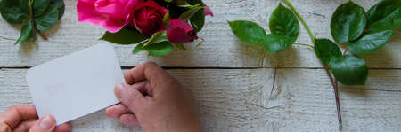 Top view of female decorator holding a  card, arranging roses on the wooden table, Concepts -...