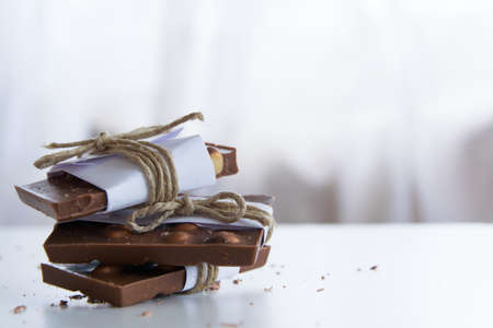 Front view of broken chocolate pieces wrapped in white paper and rustic twine on the white backgroundの写真素材