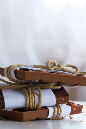 Front view of broken chocolate pieces wrapped in white paper and rustic twine on the white...
