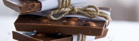 Front view of broken chocolate pieces wrapped in white paper and rustic twine on the white...