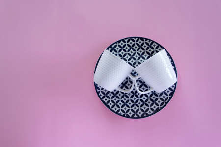 Overhead flat lay view of clean tableware (blue plate and two white coffee cups) on pink background