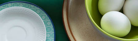 Ceramic tablewares in warm pastel colors and fresh chicken eggs on deep green backgroundの写真素材