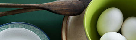 Ceramic tablewares in warm pastel colors and fresh chicken eggs on deep green backgroundの写真素材