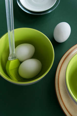 Ceramic tablewares in warm pastel colors and fresh chicken eggs on deep green background