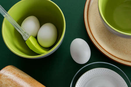 Ceramic tablewares in warm pastel colors and fresh chicken eggs on deep green backgroundの写真素材