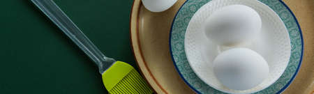 Ceramic tablewares in warm pastel colors and fresh chicken eggs on deep green background