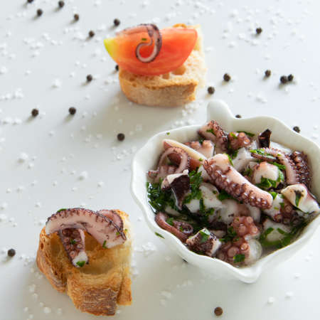 Top view of octopus salad with slices of toasted baguette - bruschetta  on white background with black pepper and sea salt. Typical Mediterranean 
appetizer foodの写真素材
