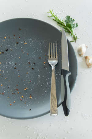 Grey empty ceramic plate with herbs knife and fork on salty white background. Minimal design. Space for text or menuの写真素材
