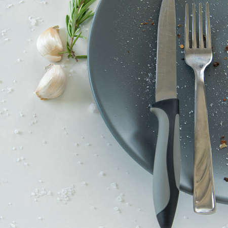 Grey empty ceramic plate with herbs knife and fork on salty white background. Minimal design. Space...