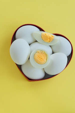 Healthy eating - eggs in heart shaped box on yellow backgroundの写真素材